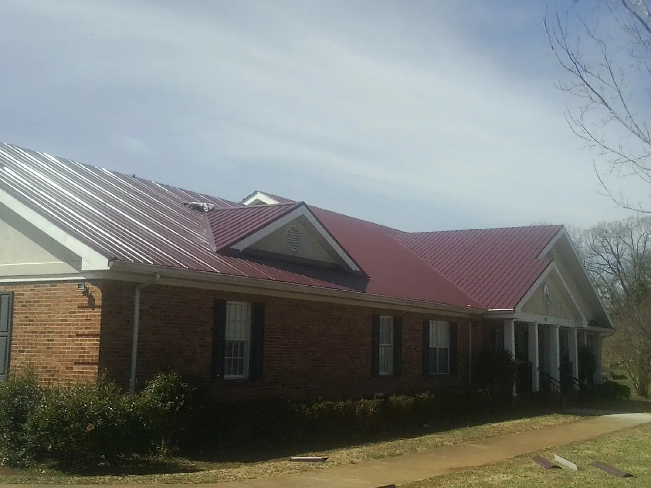 Red metal roof with gabled entries on a long brick building, from a Hail Damage Roof Repair job in Marlinton