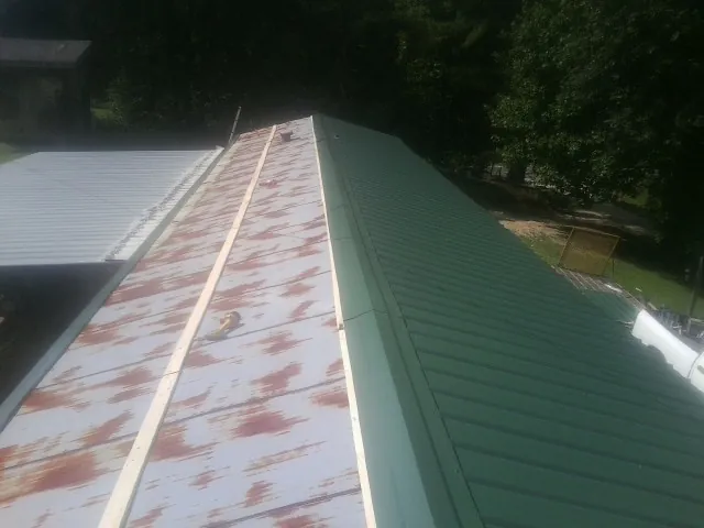 Old rusted panels beside newly installed green metal roofing — Wind Damage Roof Repair by Roofing Brothers in Marlinton