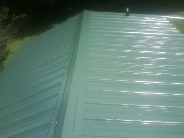 New green metal panels meeting at the ridge of a roof — Flat Roof Repair work by our crew in Marlinton