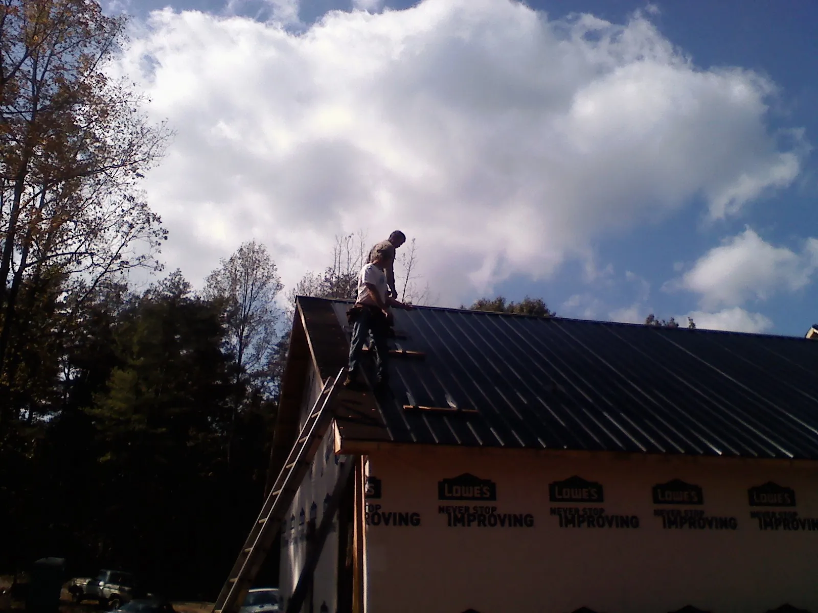 Roofer fastening dark metal panels high against a cloudy sky, from a Roof Inspection job in Marlinton