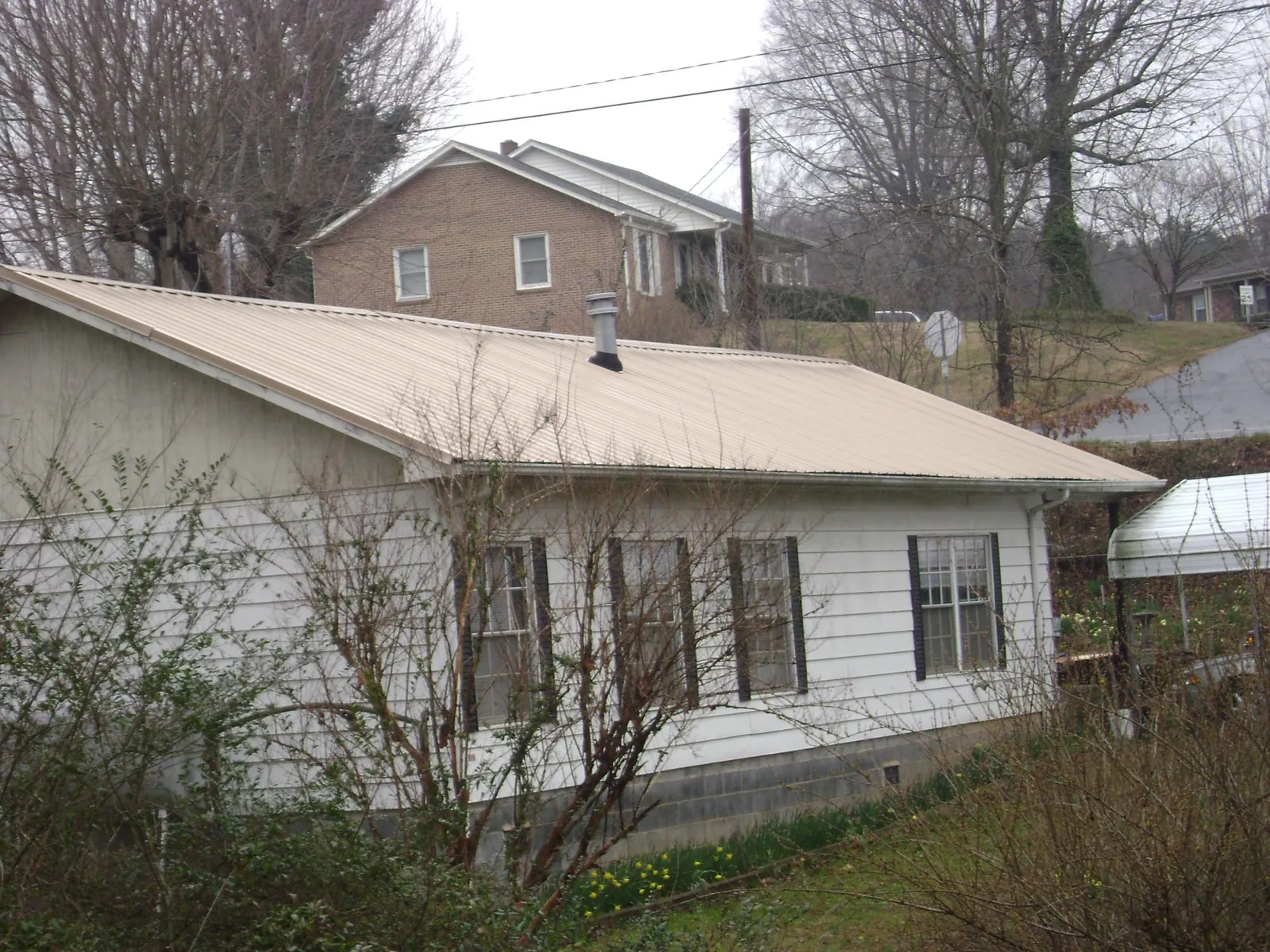 Tan metal roof on a white sided house set into a hillside — Commercial Roofing by Roofing Brothers in Marlinton