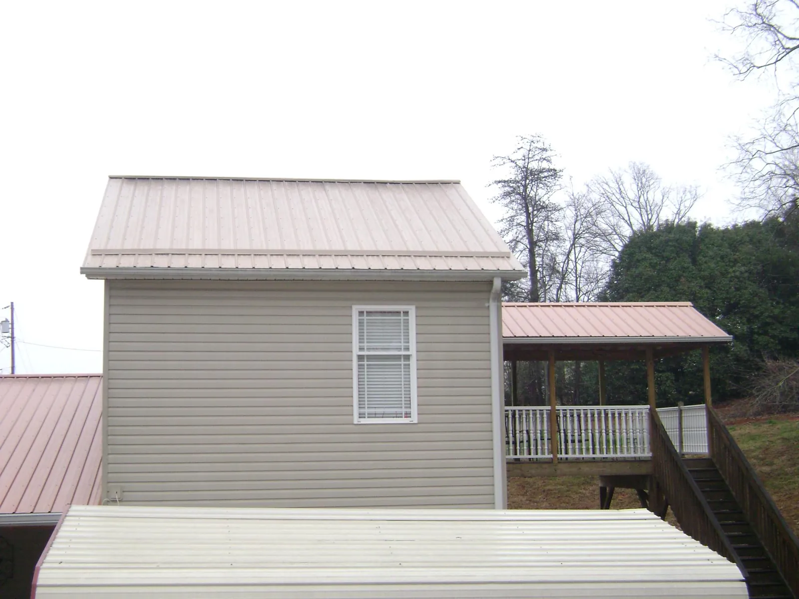 Tan metal roofs on a two story addition and attached porch, from a Roof Replacement job in Marlinton